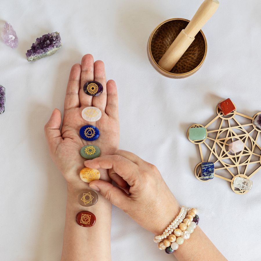 Hands, chakra stones, a singing bowl and a Metatron's cube crystal grid laid out on white linen
